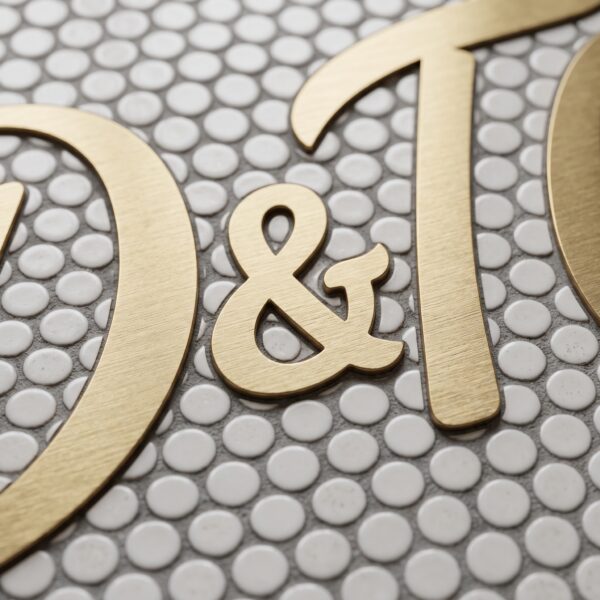 Brushed brass logo lettering inlaid into penny round mosaic